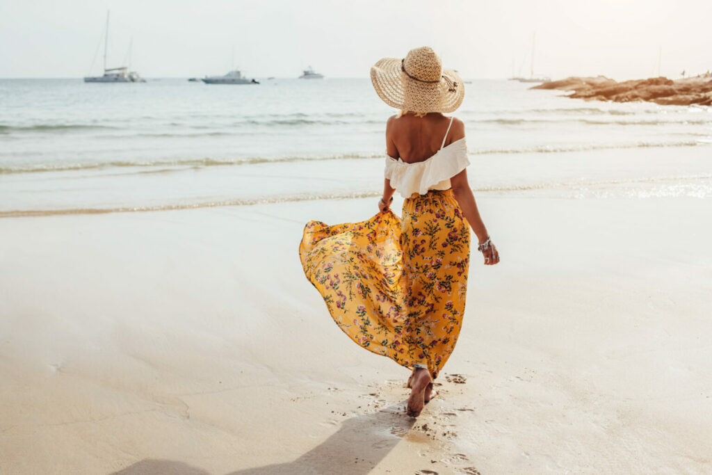 Egy virágos maxi szoknyát viselő lány sétál a homokos tengerparton