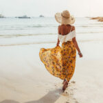 Egy virágos maxi szoknyát viselő lány sétál a homokos tengerparton