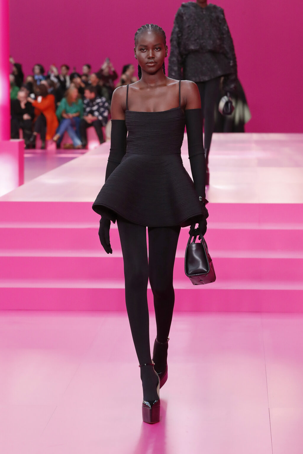 Egy modell fekete, pántos ruhában, platformos magassarkúban sétál a Párizsi Fashion Week kiuftóján