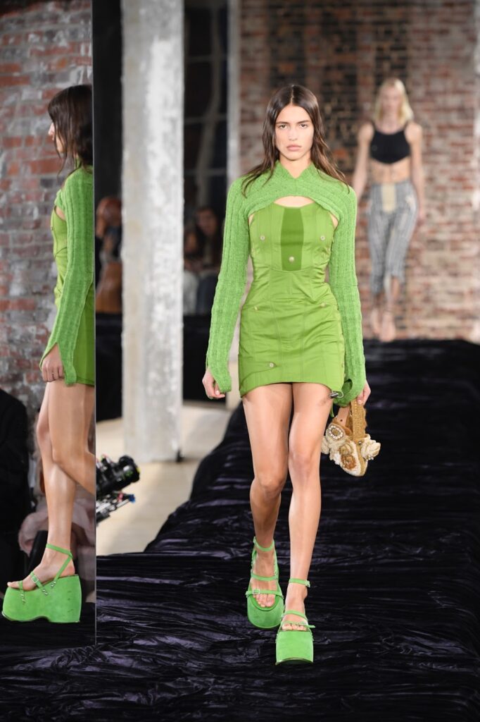 Egy modell zöld, kivágott, mini ruhában és platformos szandálban