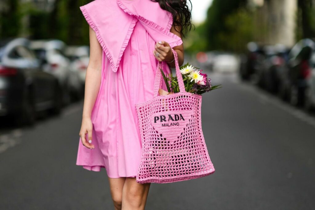 Egy női modell rózsaszín ruhában és hálós Prada táskával