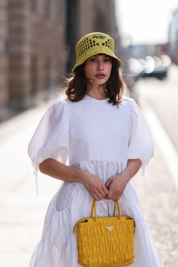 Modell egy sárga, azsúros kötött vödör kalapban és fehér ruhában