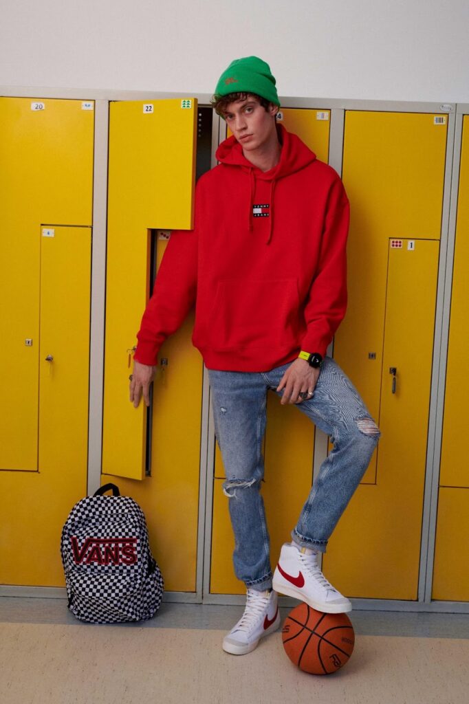 Egy fiú beanie sapkában, piros pulóverben áll az iskolai szekrénysor előtt