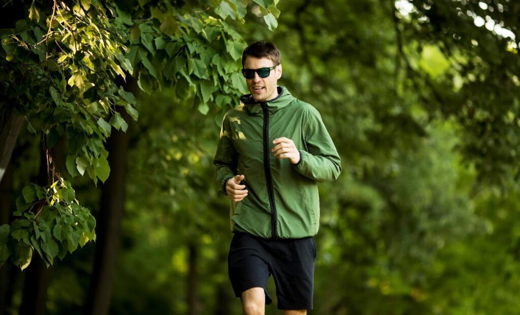 Egy zöld kabátot és rövidnadrágot viselő férfi fut a fák között