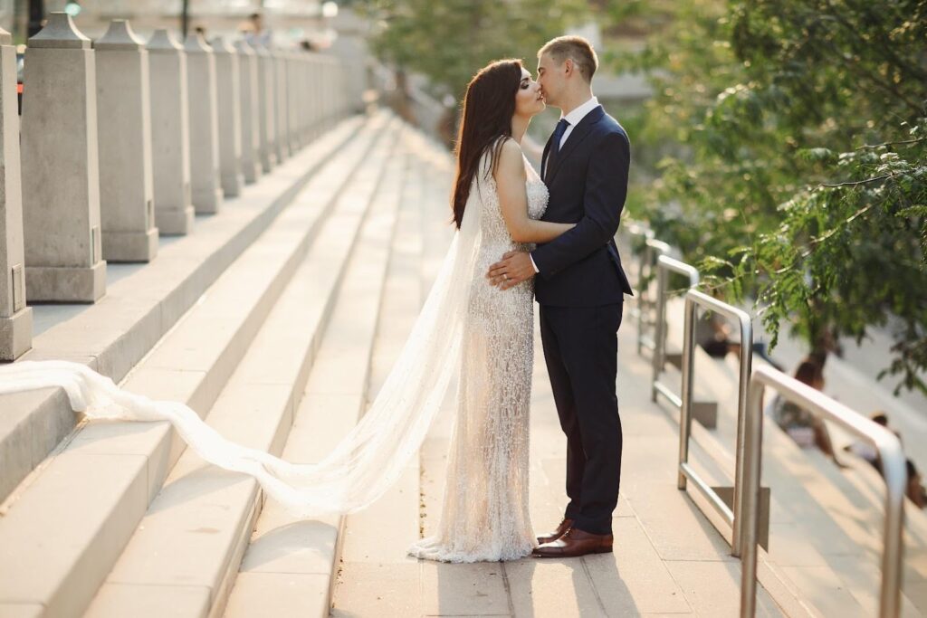 A menyasszony és a vőlegény a lépcsőn áll, a menyasszony elegáns fehér ruhában, a férfi öltönyben