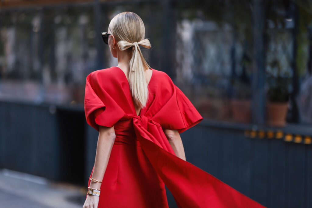 hogyan öltözzünk fel Szentestére 2023-ban - elegáns, hosszú piros ruhát viselő nő, hátul masnival