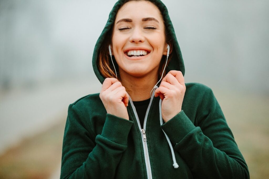 Fiatal nő zöld, kigombolt kapucnis pulóverben, fülhallgatóval a fülében