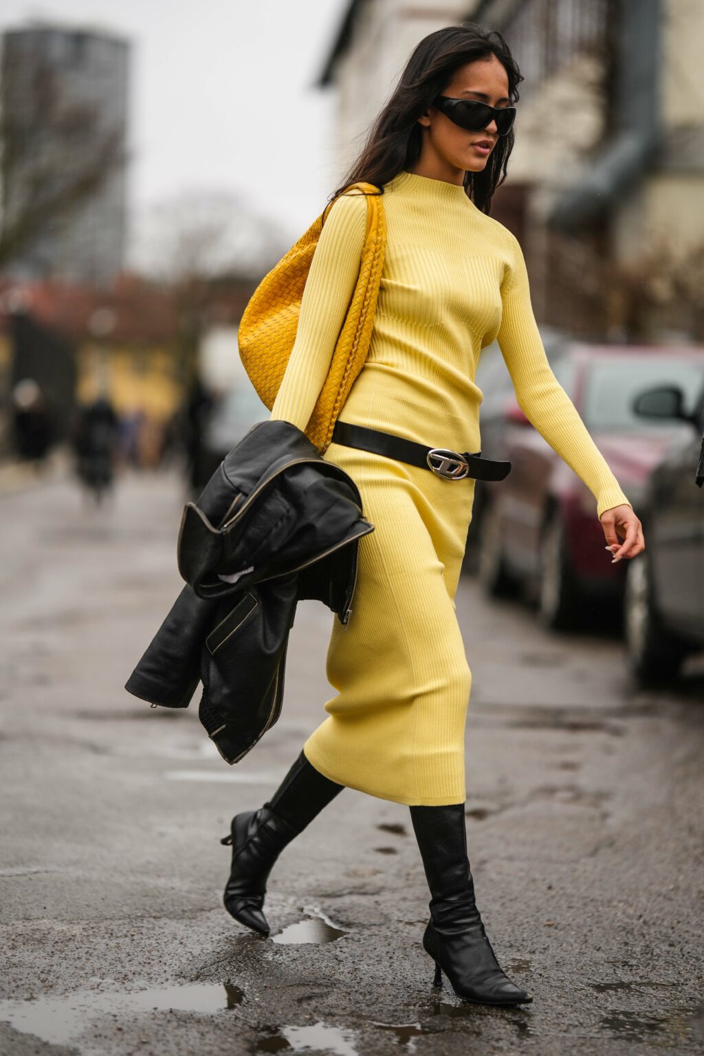 Egy vendég fekete napszemüveget, sárga, hosszú ujjú garbót, bőr válltáskát visel a 2023-as Koppenhágai Divathéten