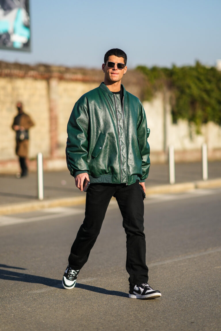 Egy vendég napszemüvegben, zöld, oversized, bőr bomberdzsekiben, fekete nadrágban és fekete-fehér nike sneakerben a 2022-es Milánói Divathéten